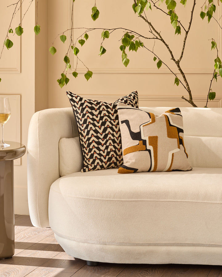 Teela medium cushion in black with geometric zigzag pattern, displayed on cream rounded sofa in styled living room.