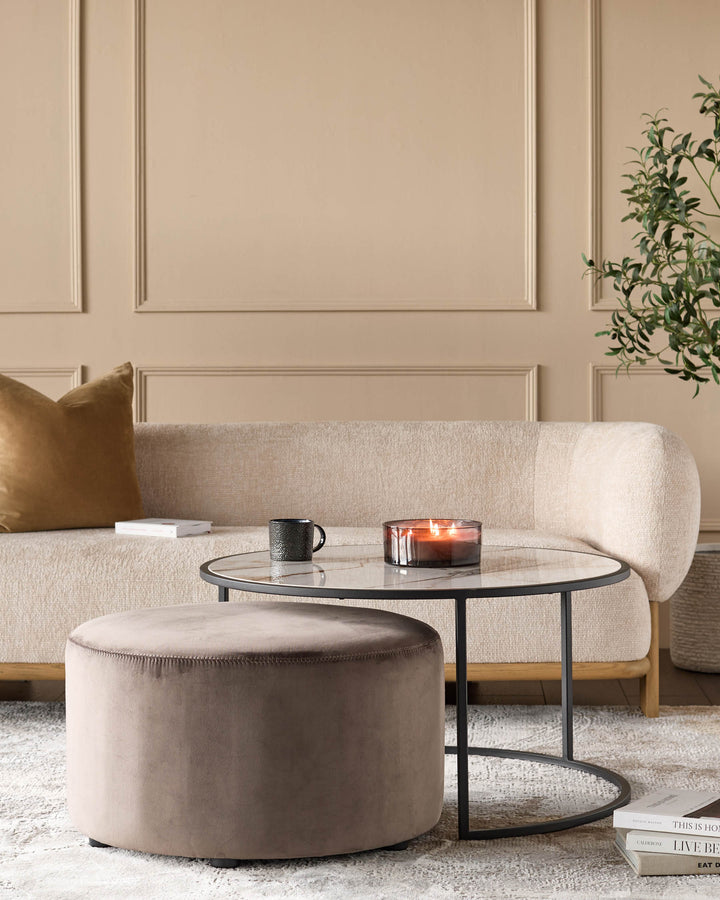Black round coffee table with marble top and matching mocha upholstered ottoman pouf in modern living room setting.