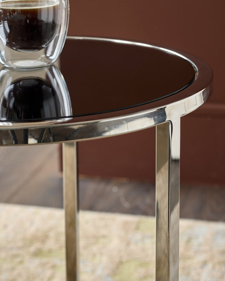 Smoked mirror tray table with brushed stainless steel frame, showing round top and angled leg detail against brown background.