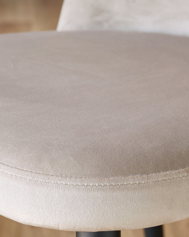 Champagne velvet dining chair close-up showing soft upholstered seat and stitched seam detail.