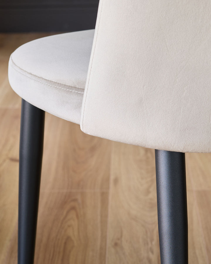 Trinny velvet dining chair in champagne, showing curved seat detail and black metal legs on wooden floor.