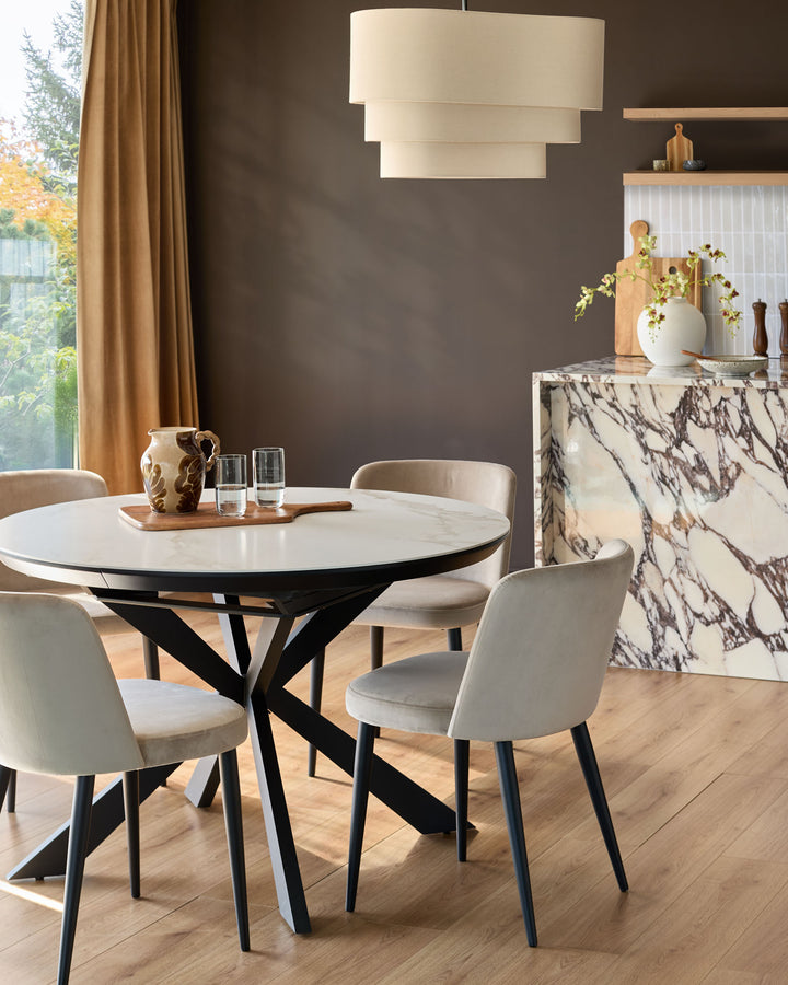 Champagne velvet dining chair with black tapered legs, shown in a styled dining room setting around a round marble table.