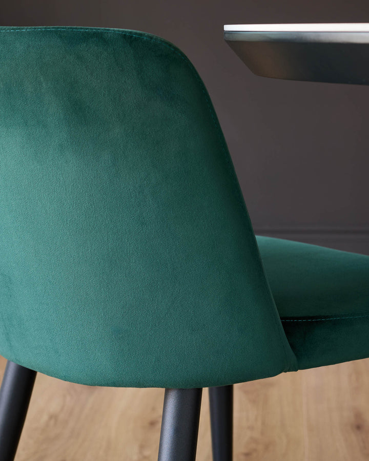 Trinny velvet dining chair in dark green, side angle showing curved backrest and black legs on wooden floor.