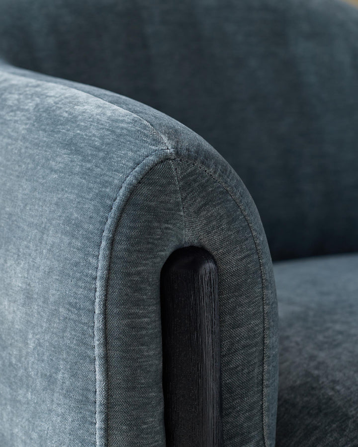 A close-up of a stylish, teal armchair with a dark wooden arm, showcasing the fabric's texture and design details.