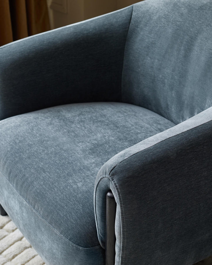 A blue velvet armchair with a low, curved back and dark wooden legs, offering a stylish and comfortable seating option.