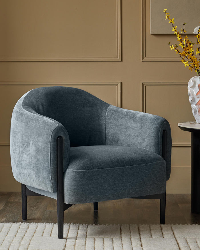 A stylish, blue velvet armchair with dark wooden legs, complemented by a patterned rug and side table.