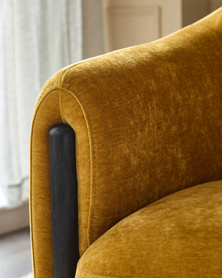 Close-up of a stylish mustard velvet chair with a curved back and black wood arm support. Luxurious and comfortable.