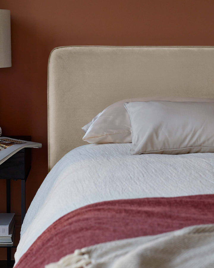 Elegant velvet bed frame with plush pillows, a textured white bedspread, and a sleek black nightstand.