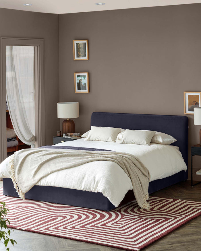 A stylish bedroom setup featuring a navy upholstered bed, complemented by a striking geometric rug and warm lighting.