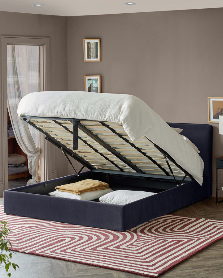 Upholstered ottoman bed frame with headboard, lifted to reveal storage space. Red and white patterned rug in the foreground.