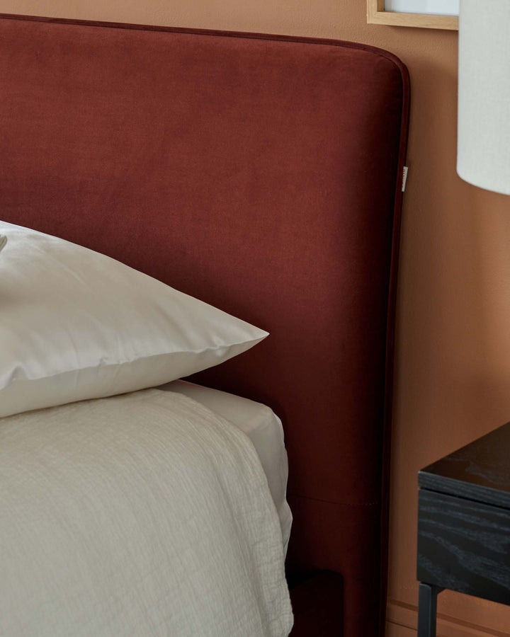 Close-up of a bed with a plush, auburn headboard, white bedding, and a black bedside table. Modern bedroom furniture.