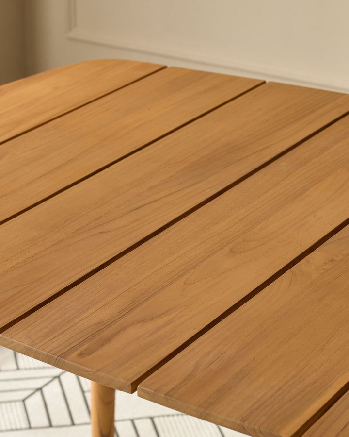 Tuscany teak wood dining table, round top with slatted surface detail, natural honey finish, angled view.