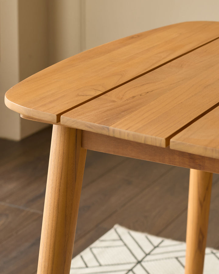 Tuscany teak dining table close-up showing smooth rounded edge, natural wood grain, and tapered wooden leg detail.