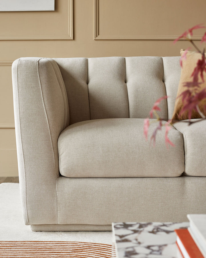 Close-up of a stylish, light-beige sofa with button-tufted back cushions and a squared-off arm.