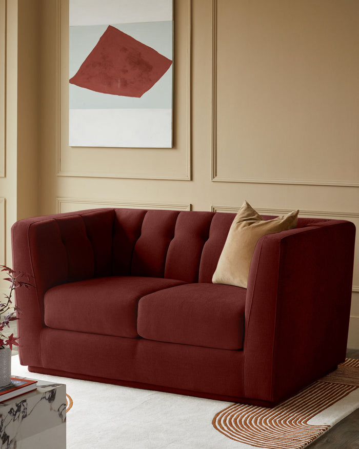 A stylish, two-seater sofa in a deep burgundy colour with a tan cushion, positioned in an elegant room.