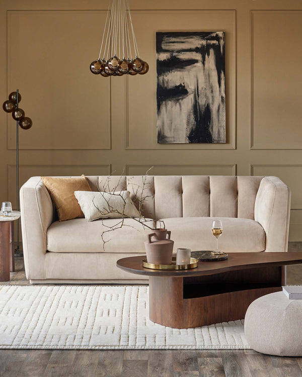 Soft beige tufted sofa with accent pillows, modern wooden coffee table, chic side table, plush rug, and stylish hanging light fixture.