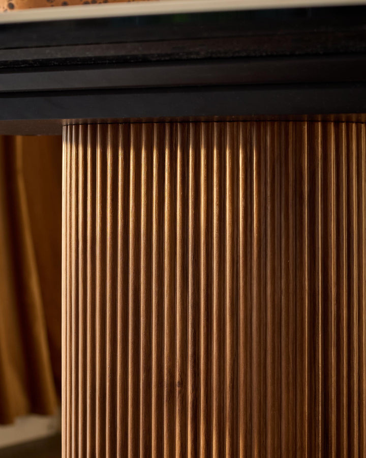Close-up of natural wood grain detail on Vidal dining table edge, showing vertical fluted texture and warm honey-brown finish.