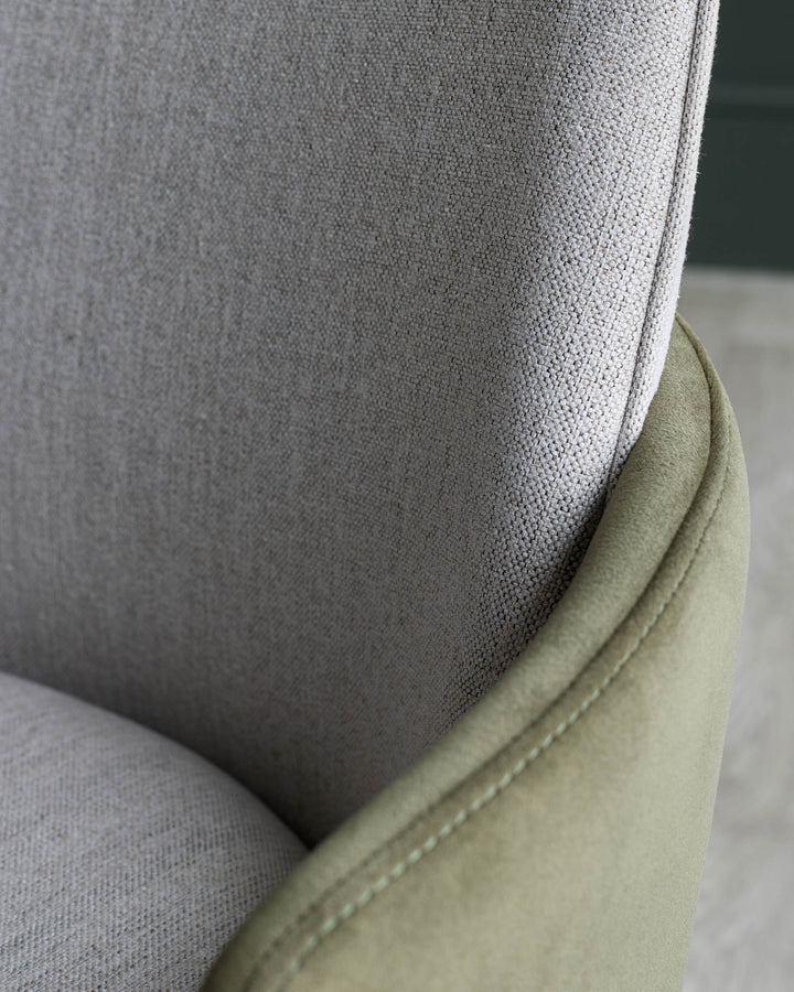 Close up of a stylish upholstered chair in neutral tones with green trim, showcasing its tactile fabrics.