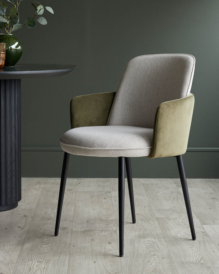 A stylish modern dining chair with a light grey fabric seat and backrest, and olive green armrests, sat on black legs.