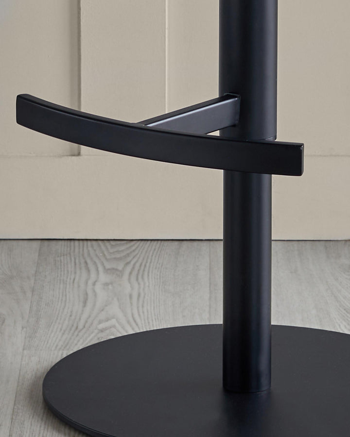 Close-up of the base of a stylish black bar stool with a round base, metal footrest and sturdy central column.