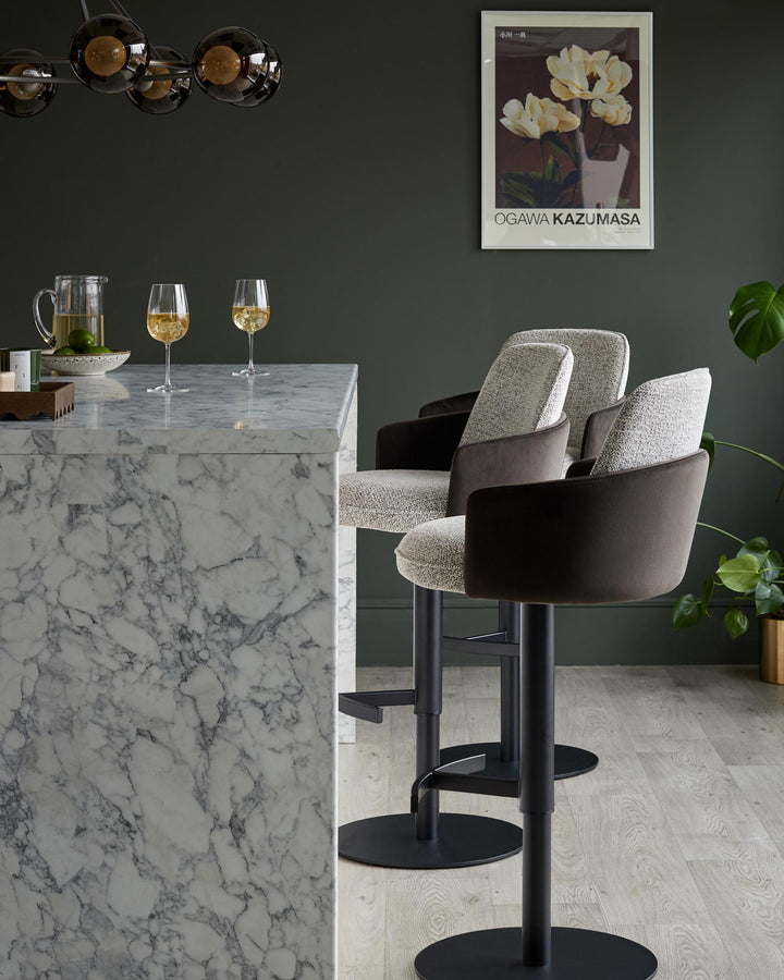 A kitchen island with marble worktop and two bar stools with a grey woven fabric seat and dark brown arms and back.