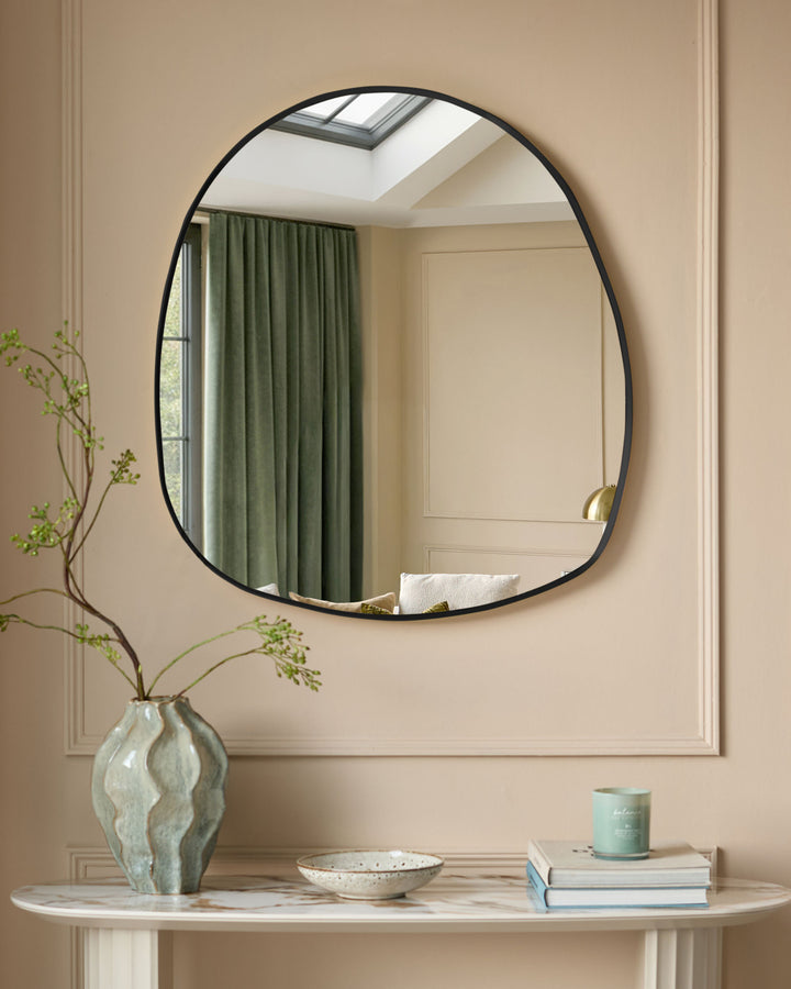 Black oval wall mirror with pebble-shaped frame, hung above marble console table with decorative accessories.