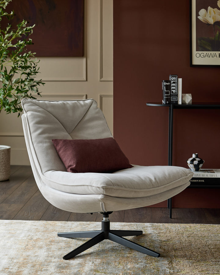 Zia swivel chair in natural grey fabric with black base, styled in a modern living room setting with burgundy wall.