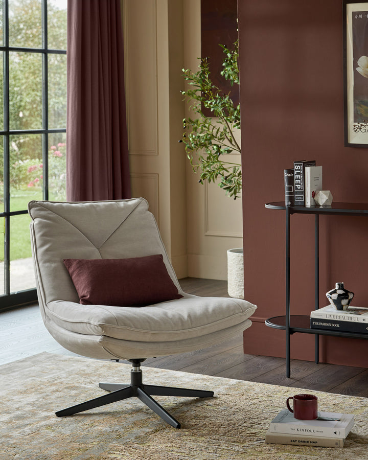 Zia swivel chair in natural grey fabric, shown in a styled living room setting with burgundy accent pillow and black swivel base.