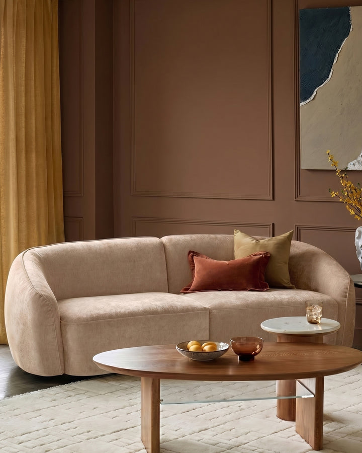 Zoey 2-seater sofa in champagne fabric with curved arms, styled with decorative pillows in a modern living room setting.