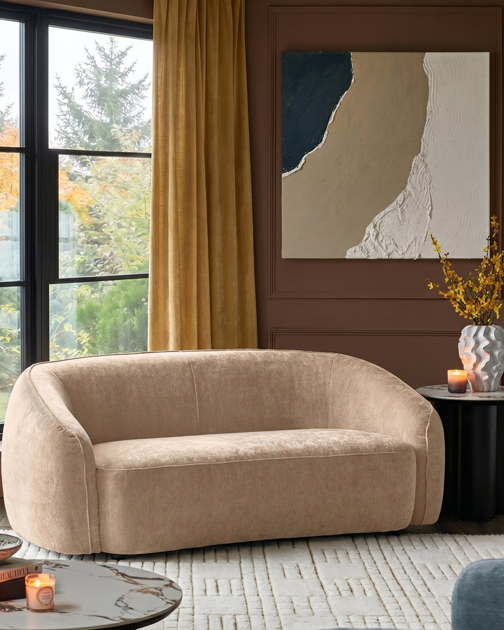 Zoey champagne fabric 2-seater sofa with curved arms and rounded silhouette in a styled living room setting.