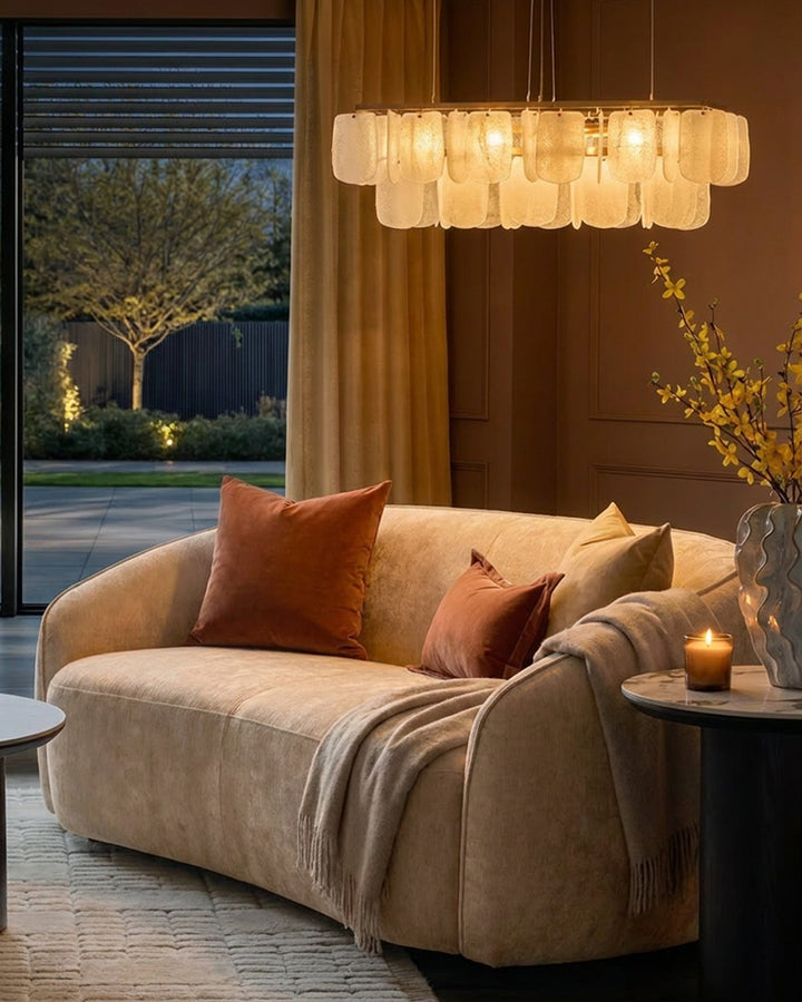 Zoey 2-seater sofa in champagne fabric with curved silhouette, styled with rust pillows and throw blanket in warm interior setting.