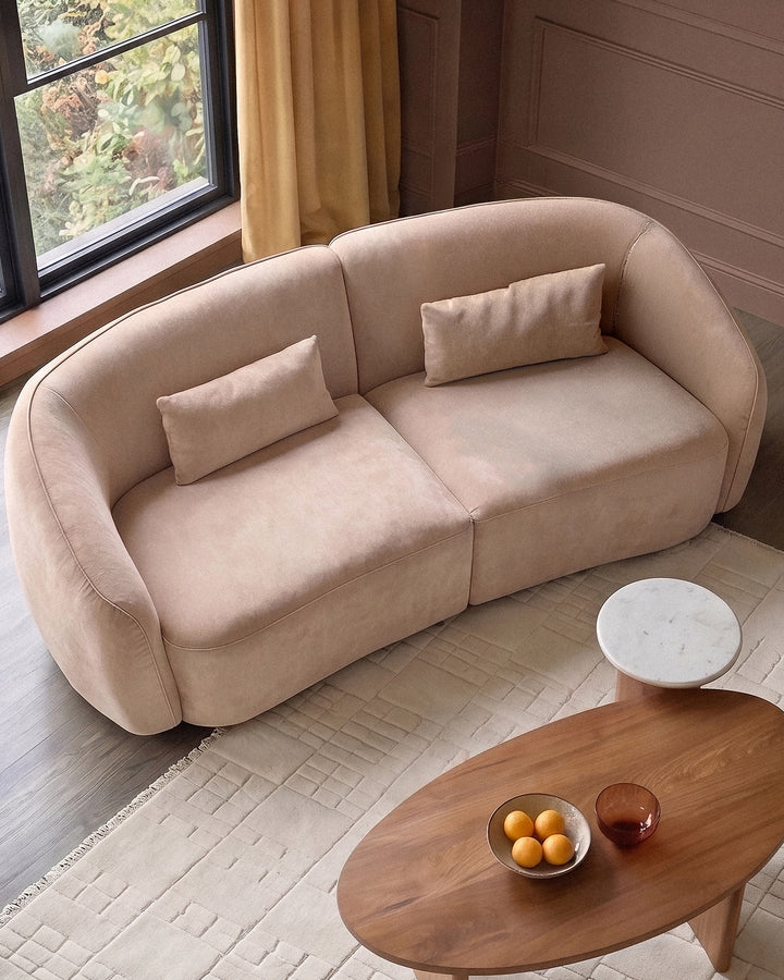 Champagne fabric 3-seater sofa with curved arms and two matching lumbar pillows, positioned in a modern living room.