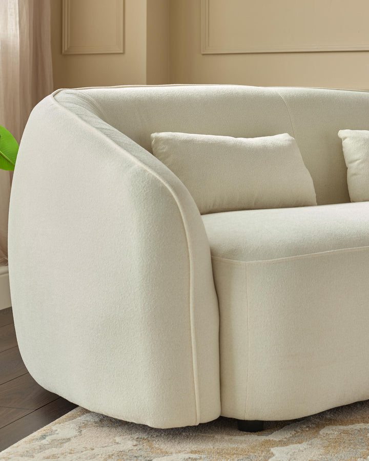 A modern, curved cream-coloured sofa with matching cushions, on a patterned rug. Minimalist design.