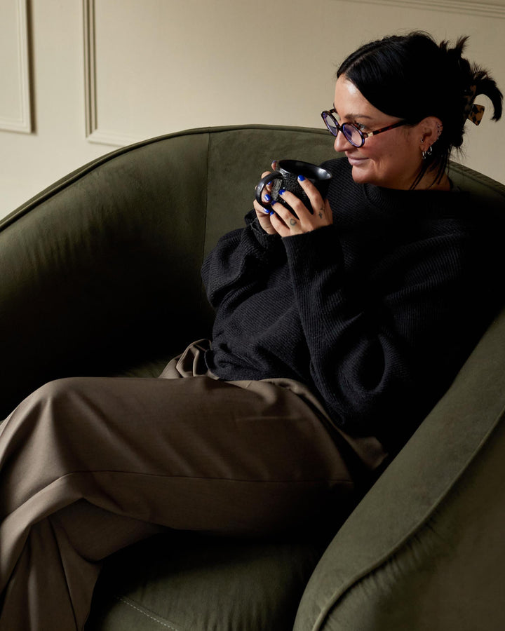 A stylish, olive-green velvet armchair provides a cosy spot to relax. The smooth, rounded design adds a touch of elegance to any living space.