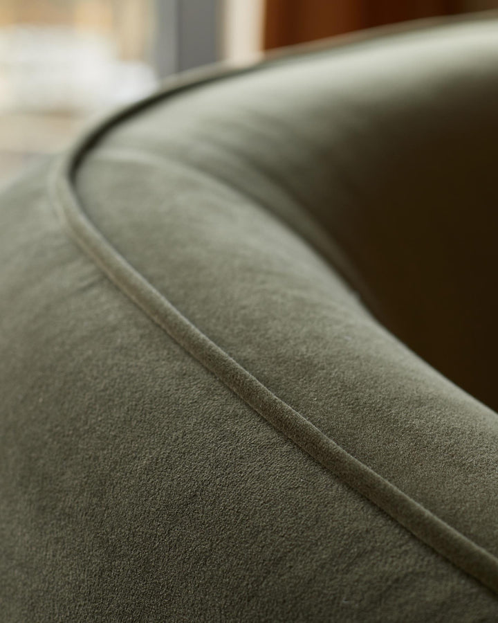 Close-up of a green velvet armchair, showcasing the plush fabric and curved design. Modern and stylish seating option.