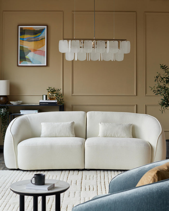 A modern living room featuring a cream sofa, glass chandelier, patterned rug, and a blue armchair.