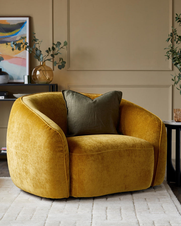A comfy gold velvet armchair with olive green cushion, sitting on a textured cream rug. Stylish and inviting furniture.