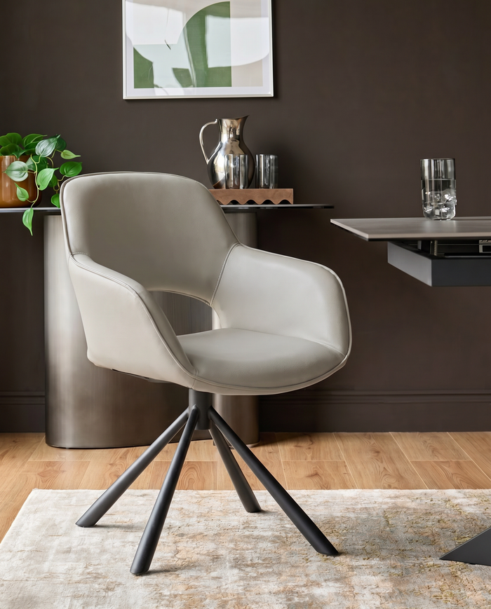 Light grey leather swivel dining armchair with curved back and black metal tripod base, shown in room setting.