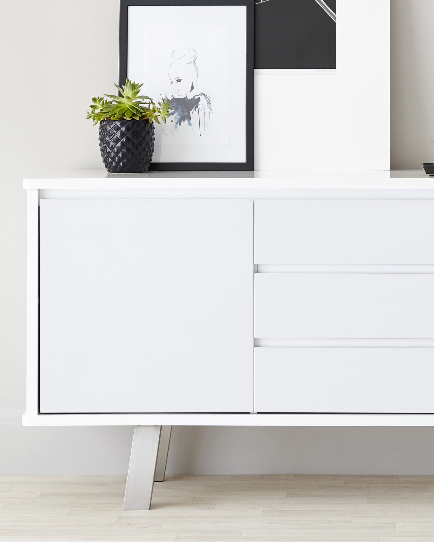 Modern minimalist white sideboard with sleek lines and metal legs, featuring two large drawers on the right side and a single large cabinet space on the left.