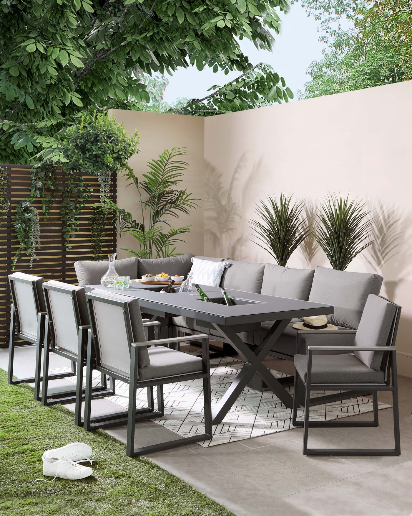 Modern outdoor furniture set featuring a sleek rectangular dining table with a matte dark finish and distinctive X-shaped legs, accompanied by six matching chairs with clean lines, durable fabric seats and backrests, all supported by a robust metal frame. The set is complemented by soft grey cushions, creating a stylish and comfortable al fresco dining experience.