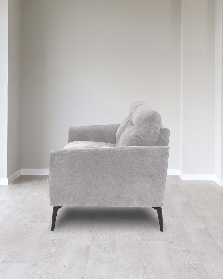 Contemporary single-seater sofa with a light grey fabric upholstery and minimalist black legs, positioned in a modern, neutral room setting.