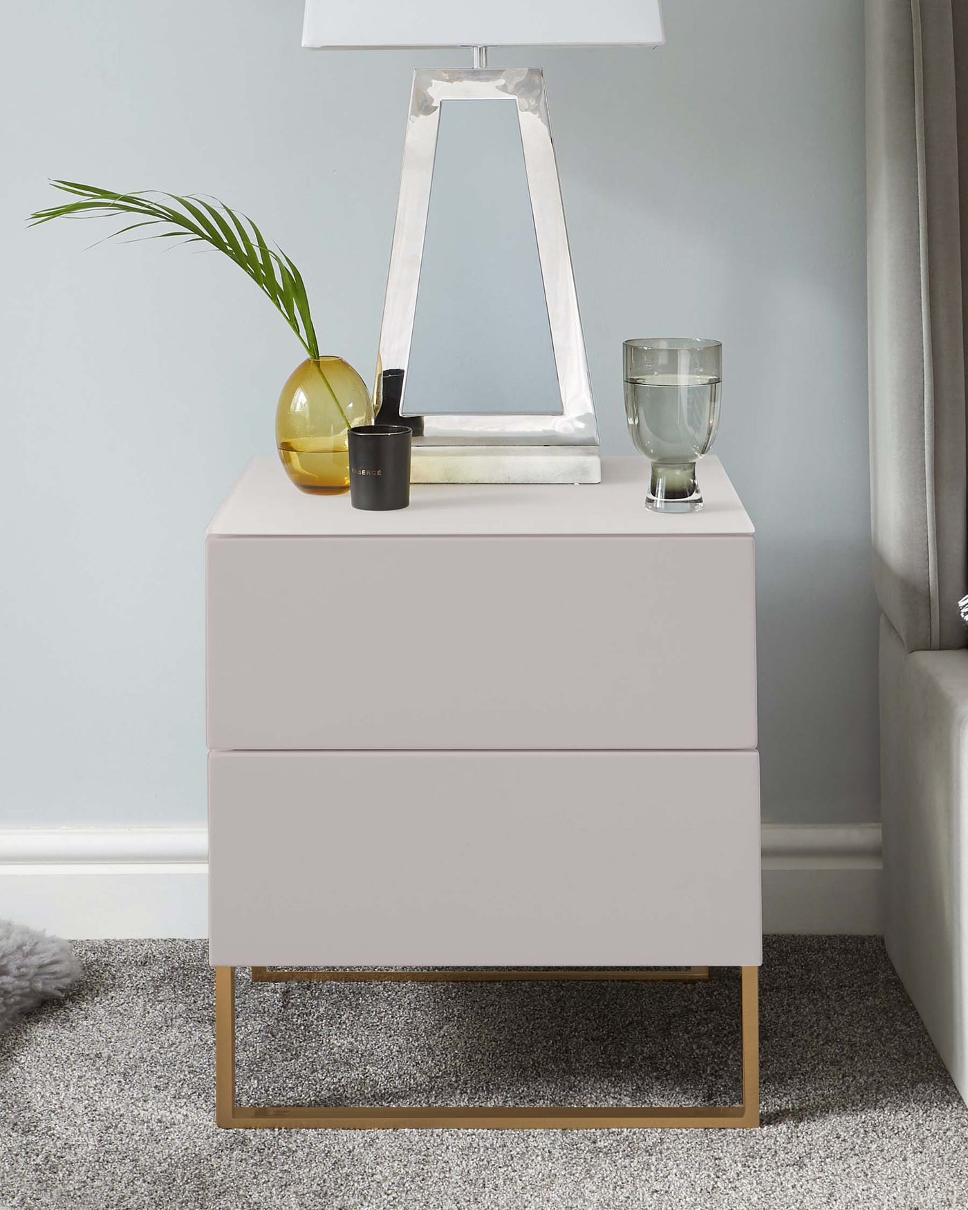 Modern light grey bedside table with two drawers and brass-coloured metal legs.