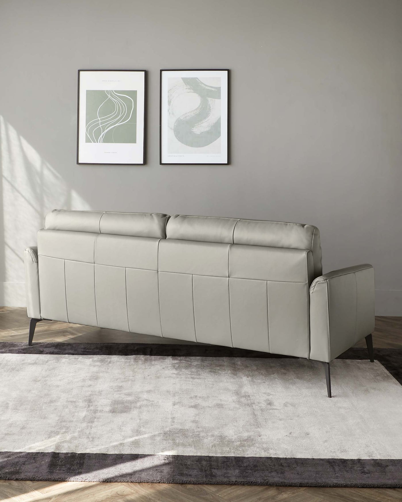 Modern light grey upholstered sofa with a linear tufted backrest and sleek metallic legs, situated on a two-toned grey area rug.