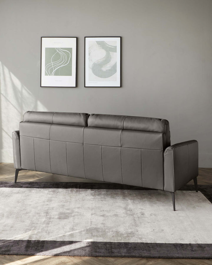 Modern three-seater sofa with sleek grey upholstery and minimalistic metal legs, positioned on a two-tone grey area rug.