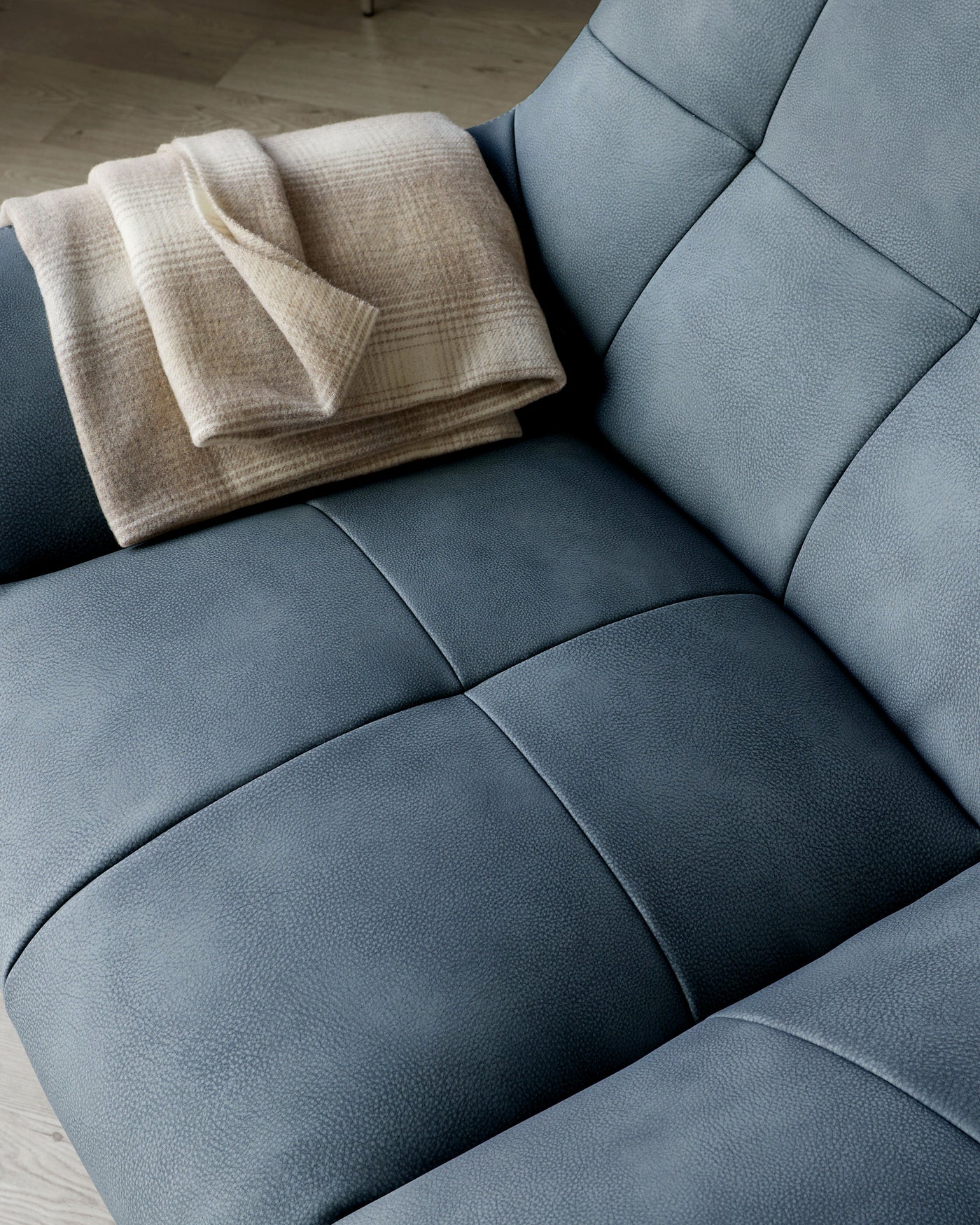 Luxurious modern blue leather sofa with a plush woven beige throw blanket neatly folded on one of its cushioned panels, featuring clean lines and a comfortable, inviting design.