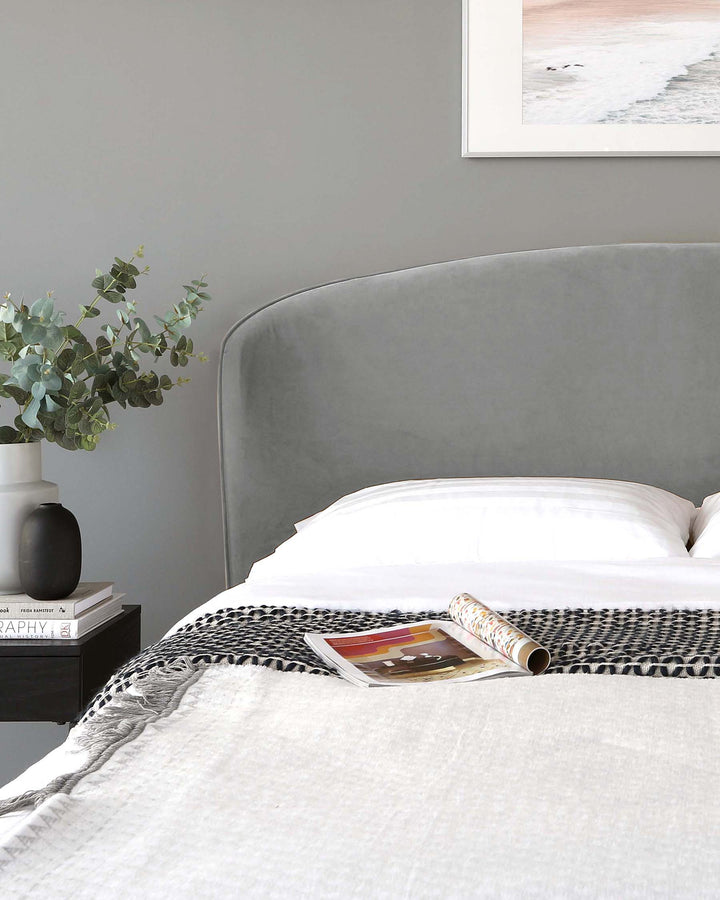 Elegant contemporary bedroom featuring a plush upholstered bed with a curved headboard in a soft grey fabric, complemented by a sleek black bedside table with clean lines and a minimalist design.