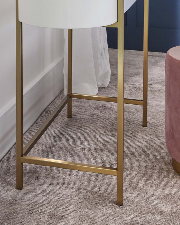 Modern minimalist furniture featuring a round white top side table with a sleek golden metal frame and a cylindrical blush pink upholstered ottoman with a plush velvet finish.