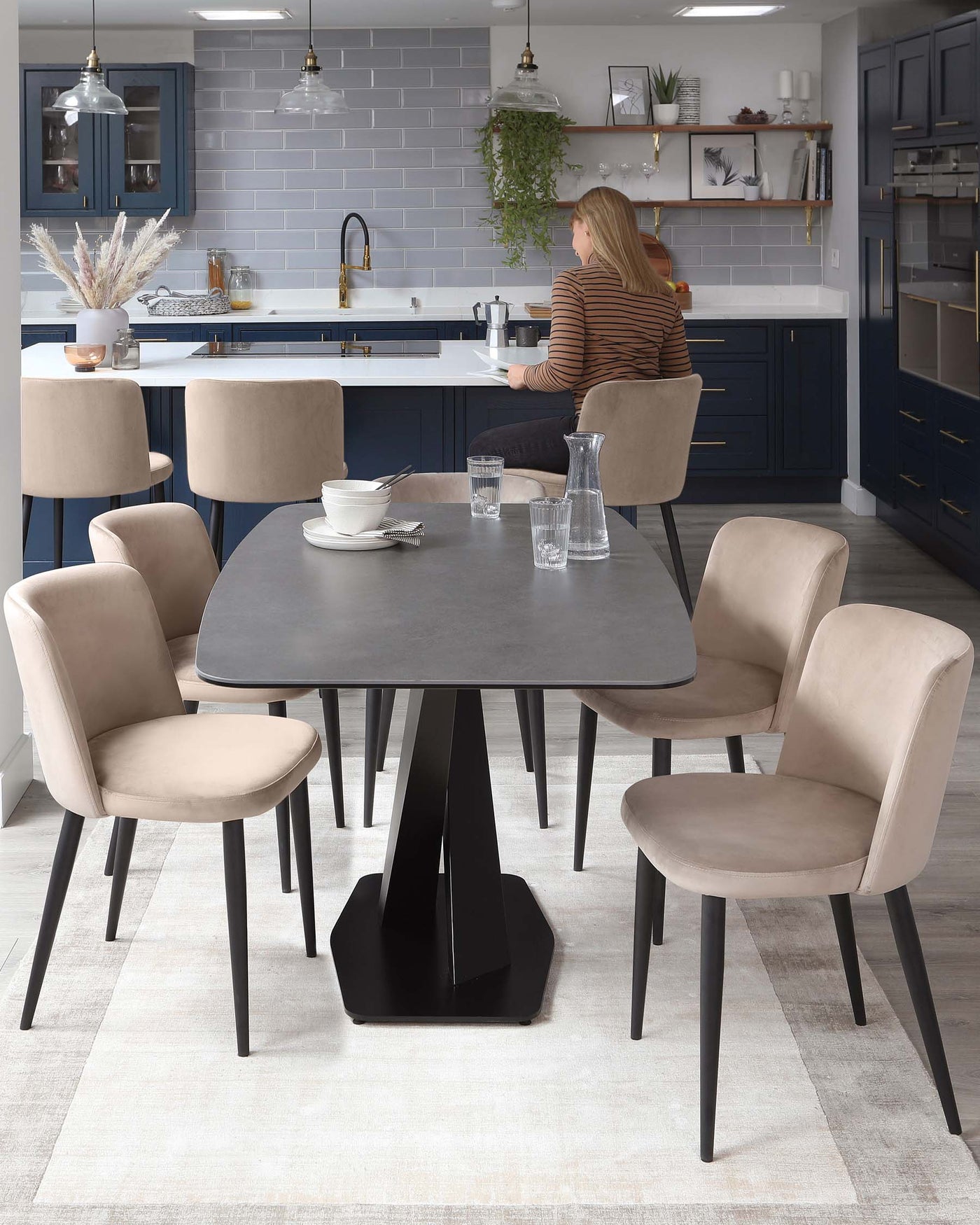 Modern dining set featuring a dark grey round table with a unique geometric black base, surrounded by four sleek upholstered chairs in a light beige fabric with slim black legs on a textured off-white area rug.