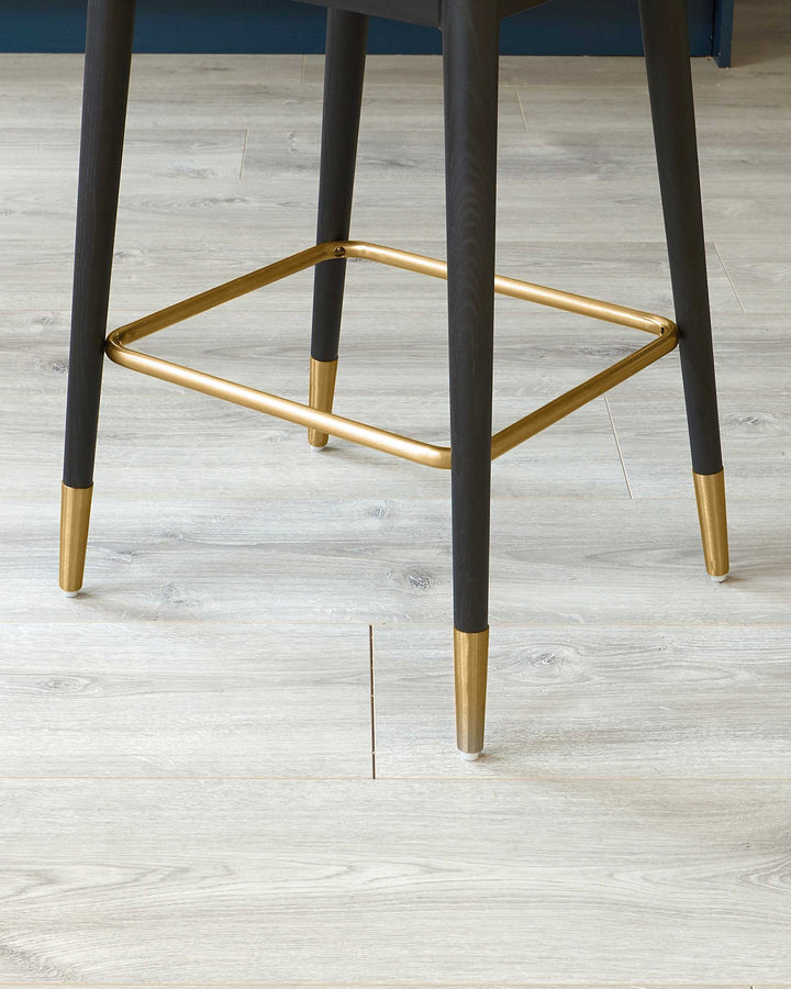 Modern chair with dark charcoal legs featuring elegant gold-coloured tips, complemented by a matching gold footrest. The chair is set against a backdrop of light wood flooring.