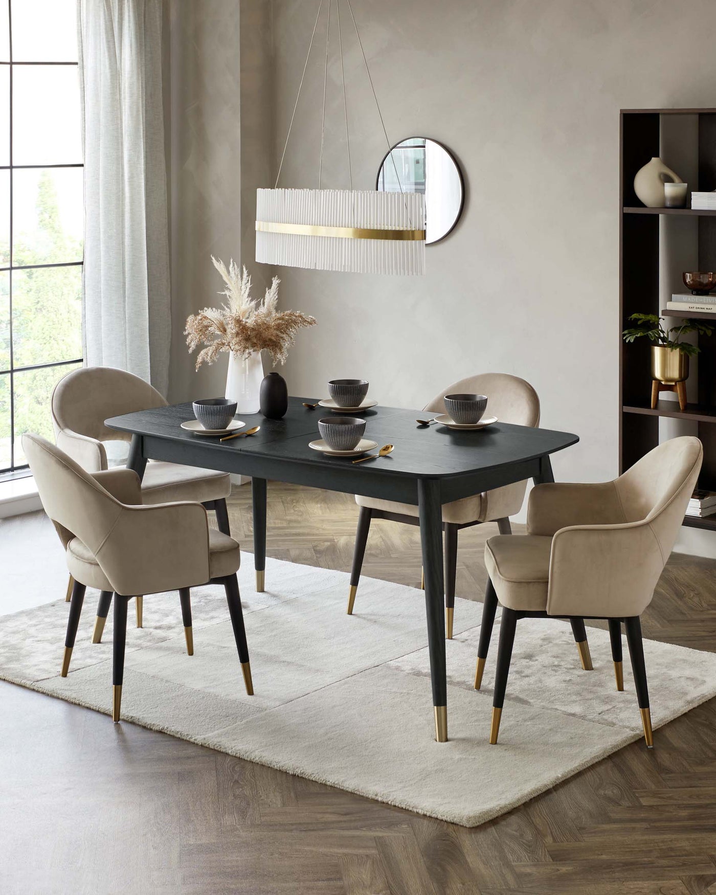 Elegant dining room furniture set featuring a rectangular matte black table with tapered legs accentuated with gold tips, surrounded by four plush beige upholstered chairs with curved backrests and gold accents on the legs. The set sits on a large off-white area rug, providing a sophisticated and modern aesthetic.